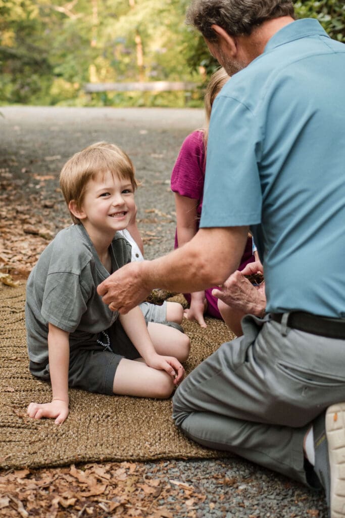 A little boy smiles at the camera while his grandfather shows him a stick at Whip Hill Park in Stoneham. 