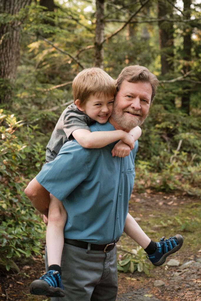 A boy is on his grandfathers back and they smile at the camera.