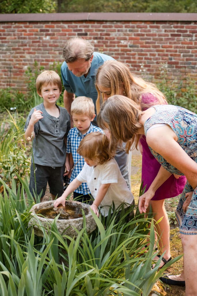 Grandparents look at a birdbath with their grandkids and one grandson smiles at the camera.