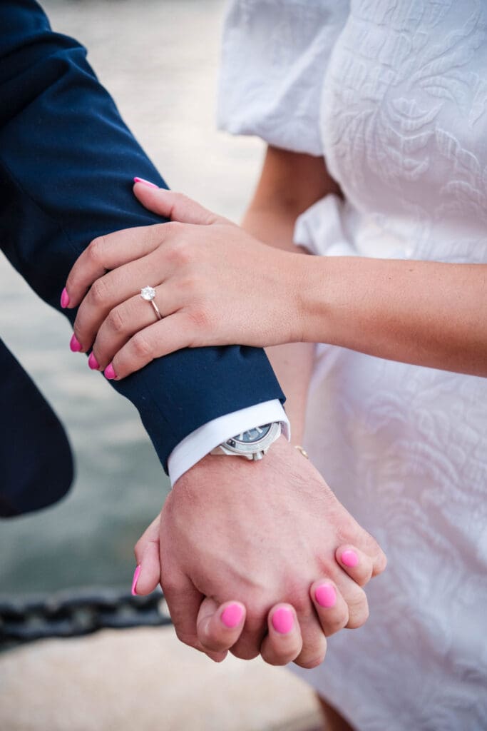 A hand resting on a mans suit shows a shiny engagement ring.