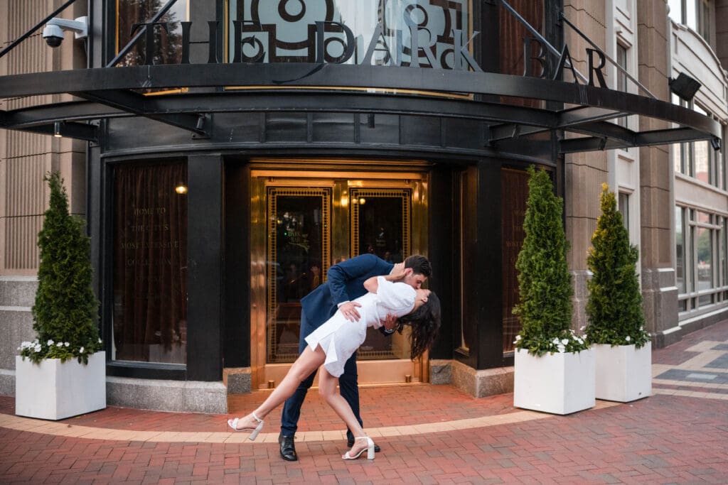 A couple kisses after they get engaged in front of The Dark Bar of the Boston Harbor Hotel.