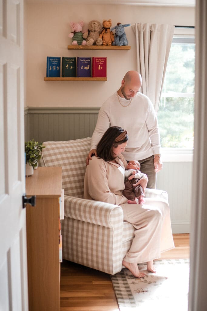 A Wakefield newborn photographer captures a couple in their nursery looking down at their newborn as they sit in a glider in this North Shore newborn session.