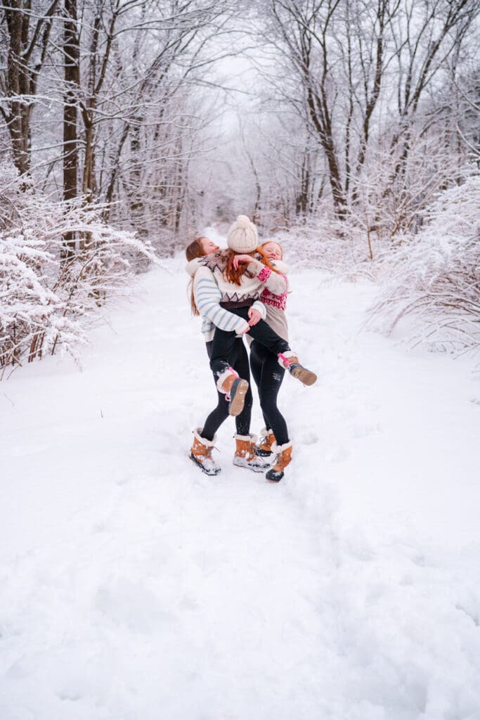 North Shore photographer captures a snowy scene where a younger child jumps into the arms of her two older sisters.