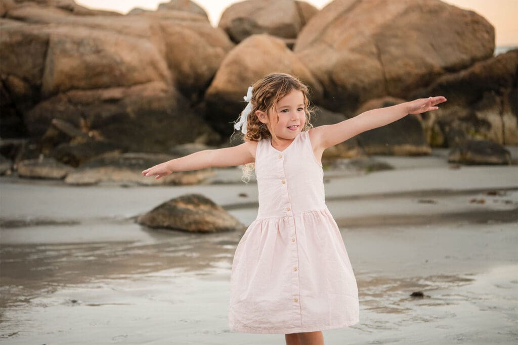 North Shore photographer captures a little Girl on Wingaersheek beach standing with her arms out like she is flying.
